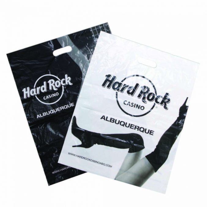 Two plastic bags with cutout handles, featuring Hard Rock Casino Albuquerque logos. One bag is black with white text, and the other is white with black text. A partial image of a person holding both bags is visible.