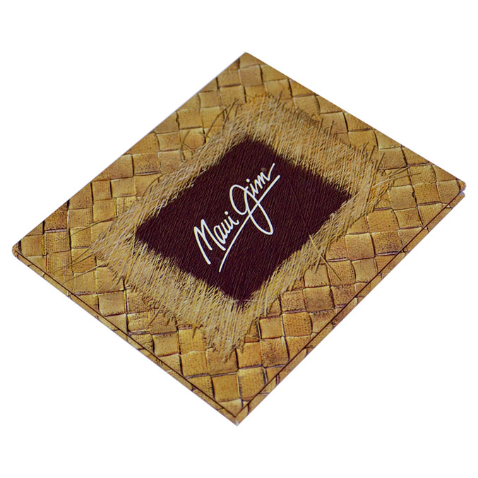 A square woven bamboo coaster with a dark brown central patch featuring the white script logo Maui Jim. The design is textured, resembling a natural woven pattern.