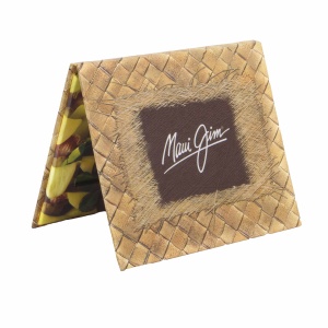 A folded cardboard display with a woven texture houses gift card packaging, featuring the white signature logo of Maui Jim on a dark brown rectangular background. The side view reveals colorful leaf patterns on the interior surface.