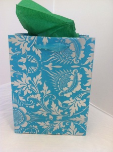 A blue gift bag with an intricate white floral pattern, elegantly filled with green tissue paper made from hand-made papers.