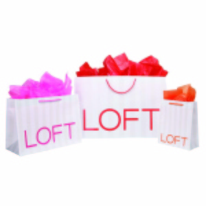 Three white shopping bags with the word LOFT in red letters stand proudly, showcasing their chic style. They vary in size and are filled with vibrant colored tissue paper—pink in the smaller ones and red in the larger one—all made from post-consumer waste materials.