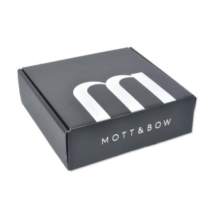 A sleek black box made from corrugated cardboard, with white text on the lid showcasing a large stylized letter M and the brand name Mott & Bow. The box remains closed, set against a pristine white background.