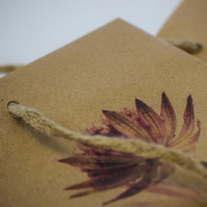 Close-up of a brown paper bag crafted from high-quality paper, featuring a floral design in shades of red and purple. The bag boasts sturdy, twisted rope handles.