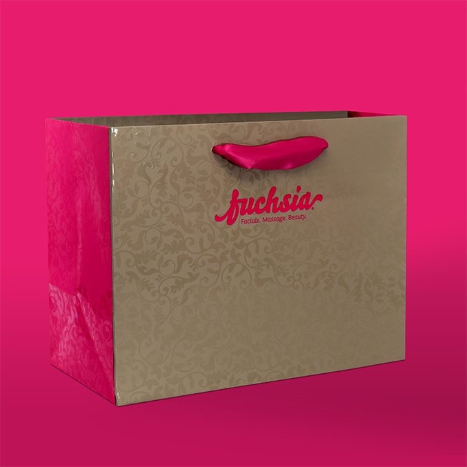 A decorative shopping bag with an ornate pattern and pink sides. It has pink fabric handles and the word fuchsia printed in pink on the front, set against a vibrant pink background.
