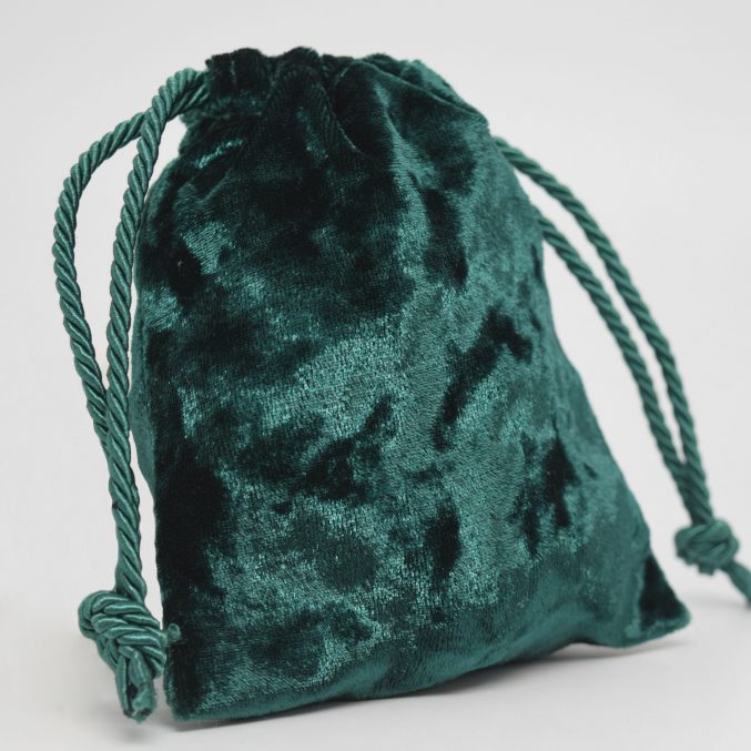 A small, green velvet drawstring pouch with twisted cord handles, partially closed at the top.