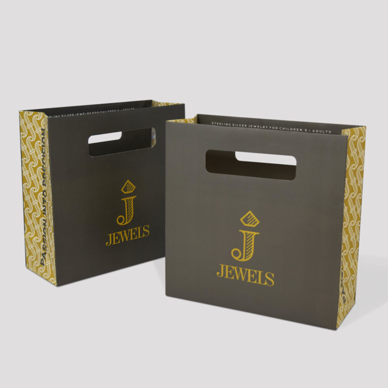 Two black shopping bags with cutout handles, featuring the golden text J Jewels and a geometric pattern on the sides. The design is modern and elegant, suitable for jewelry branding.