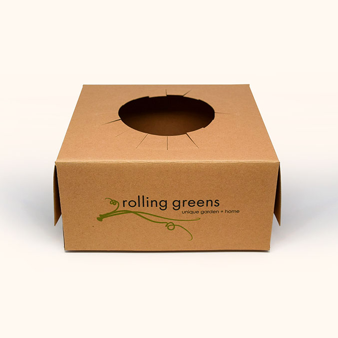 A brown cardboard box with rolling greens and unique garden + home printed on it in green text. The box has a round opening on the top.