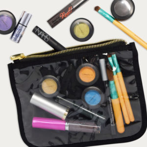 A clear makeup bag, perfect for home storage, holds various beauty essentials like lipsticks, brushes, and eyeshadows. More products scatter around, featuring a mascara and vibrant single eyeshadow pots in assorted colors.