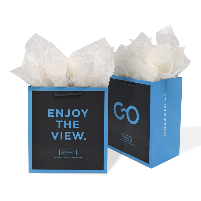 Two blue shopping bags with black panels, featuring bold text ENJOY THE VIEW and GO in white and blue font. The bags are filled with light-colored tissue paper and have rope handles.