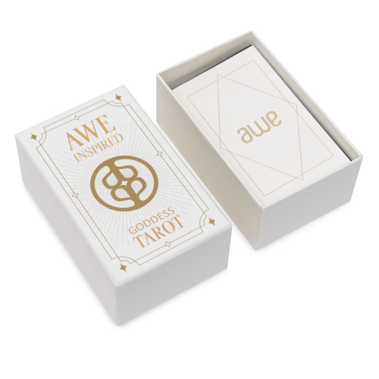 A set of tarot cards titled Awe Inspired Goddess Tarot. The open box reveals the top card with awe printed on it. The design features a gold geometric pattern and elegant typography.