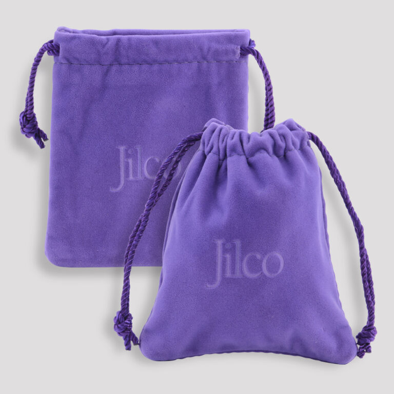 Two purple velvet drawstring pouches, each with Jilco embroidered in white. One pouch is larger and flat, while the other is smaller and has a rounded shape. The drawstrings are tied, and the background is light gray.