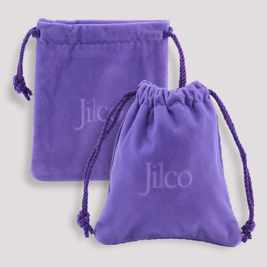 Two purple velvet drawstring pouches, each with Jilco embroidered in white. One pouch is larger and flat, while the other is smaller and has a rounded shape. The drawstrings are tied, and the background is light gray.