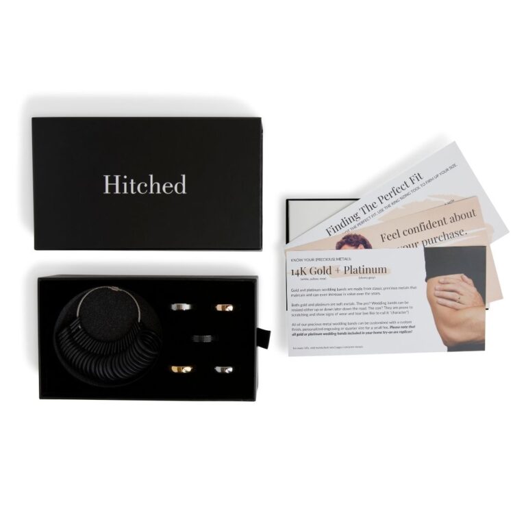 An open black box labeled Hitched, designed as a custom rigid box, displays two silver rings alongside a ring sizer. Beside this elegant packaging are informational cards about ring fit and materials, featuring images of hands adorned with rings and details on gold and platinum.
